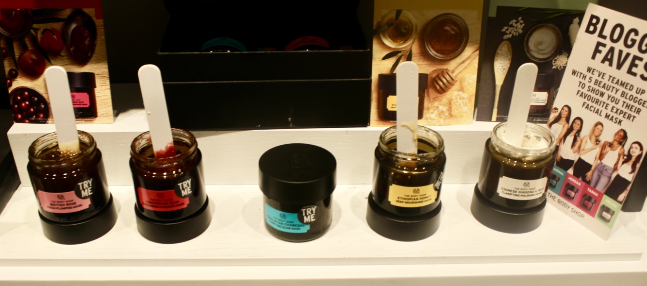 five circular black pots full of face masks and some white lolly sticks on a white shelf with a card that has blogger favourites written in bold black writing on it, on a bright background.