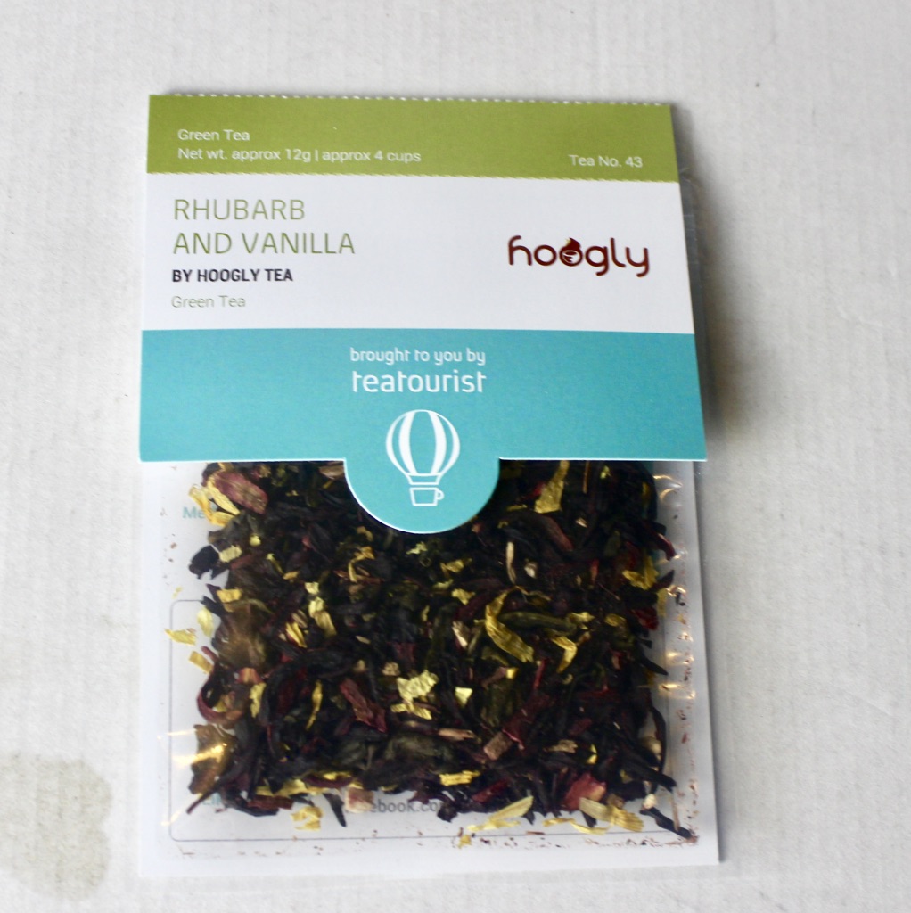 Tea Tastes Terrific | Teatourist June 2017 A square clear plastic bag containing some dark brown tea leaves with a cardboard label that has Rhubarb And Vanilla written in light green writing and Hoogly Tea written in smaller brown writing on it, on a white background.