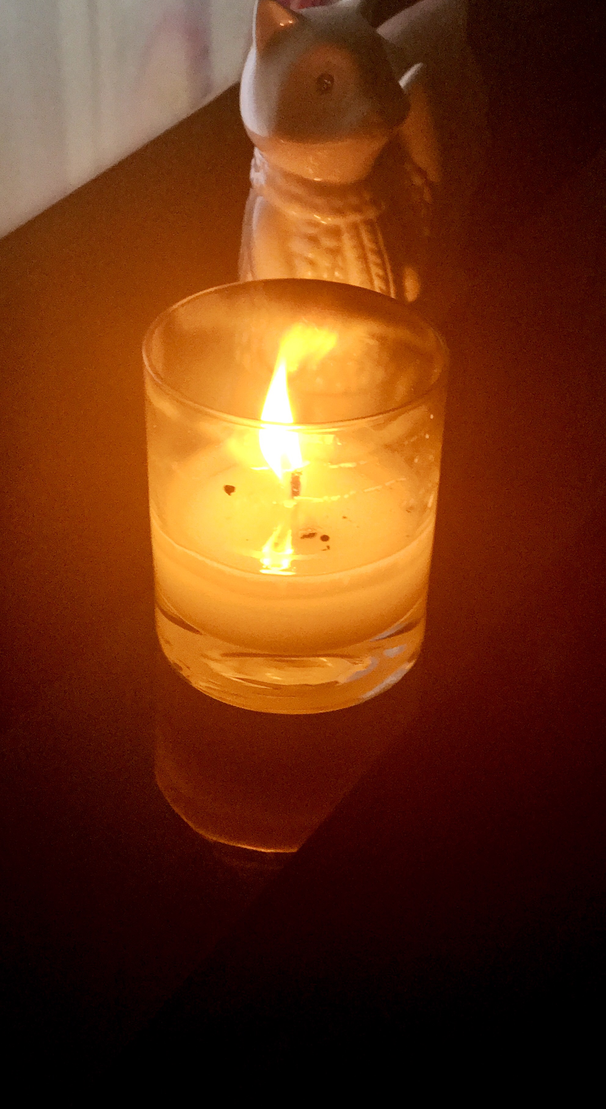 The Best Candle For You | Candles Just 4 You Lemongrass and Verbena Candle A large glass jar full of some cream coloured wax with an orange coloured flame on a clear glass table, on a light background.