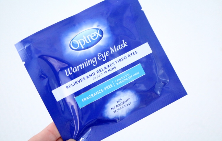 A small blue plastic pouch with a light blue oval logo that has optrex written in bold white writing and warming eye mask written in italic cursive white writing on it, on a white background.