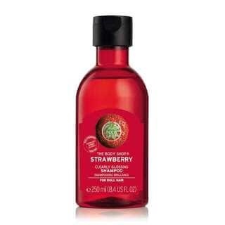 Sweet Sweet Strawberries | The Body Shop Strawberry Clearly Glossing Shampoo and Conditioner A tall cylindrical plastic bottle full of some bright cherry red liquid with a clear label that has a circular picture of a strawberry and The Body Shop Strawberry Clearly Glossing Shampoo written in bold white writing on it, on a white background.