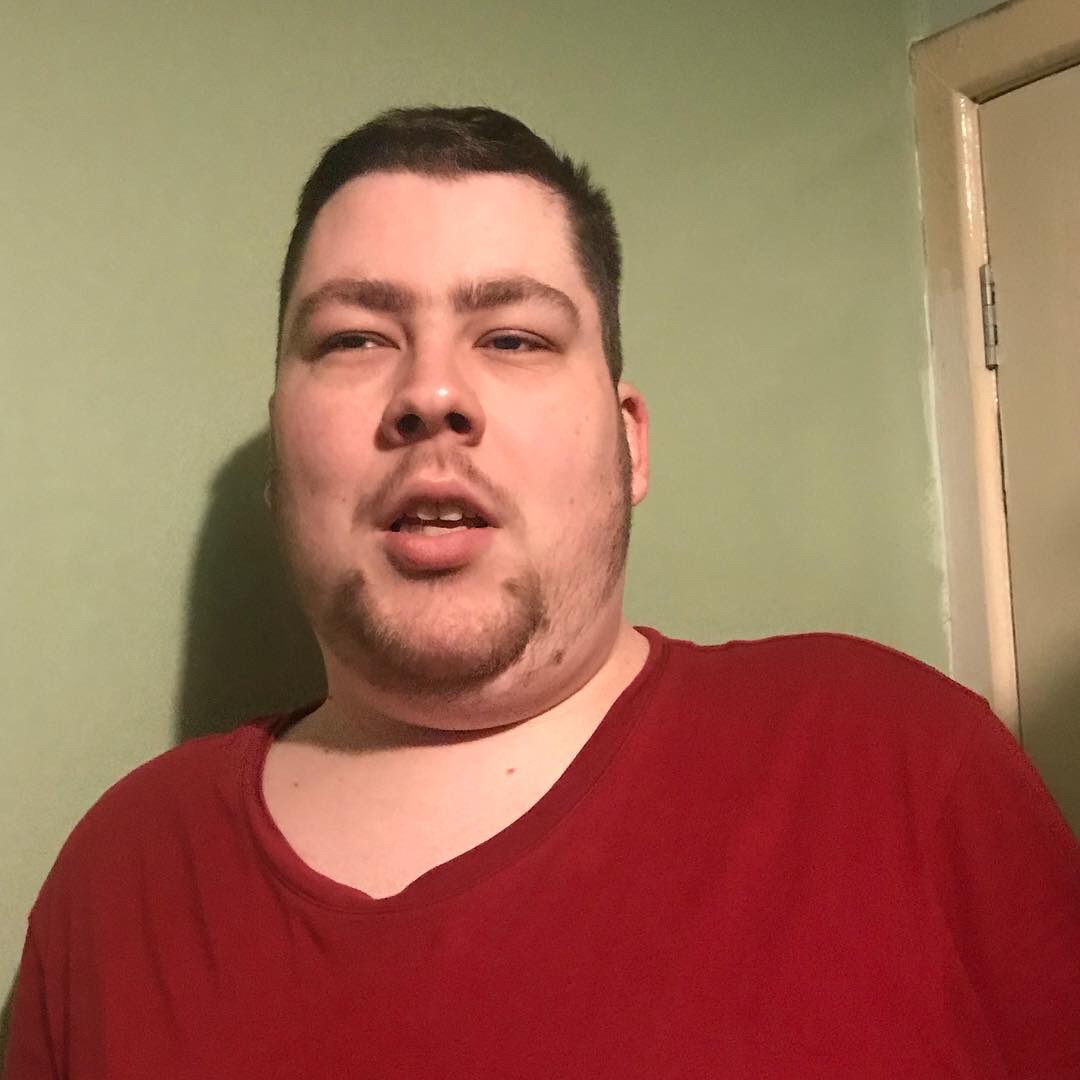 A close up of me stood wearing a bright red t-shirt with my mouth open, on a light background.