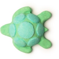 A green turtle shaped bath bomb that has some dark green patches on it's Shell, on a white background.