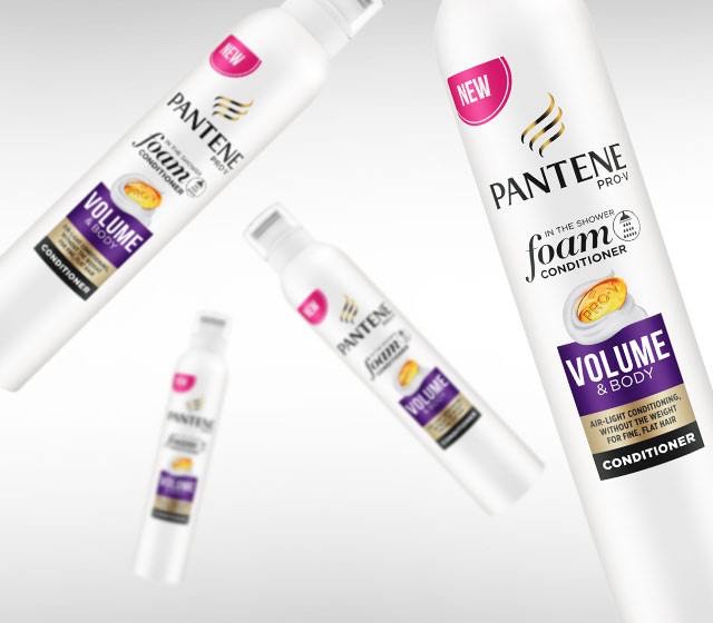 A tall cylindrical silver metal bottle with a white lid and a purple label that has Pantene Pro-V Volume & Body Foam Conditioner written in bold white writing on it, on a white background.