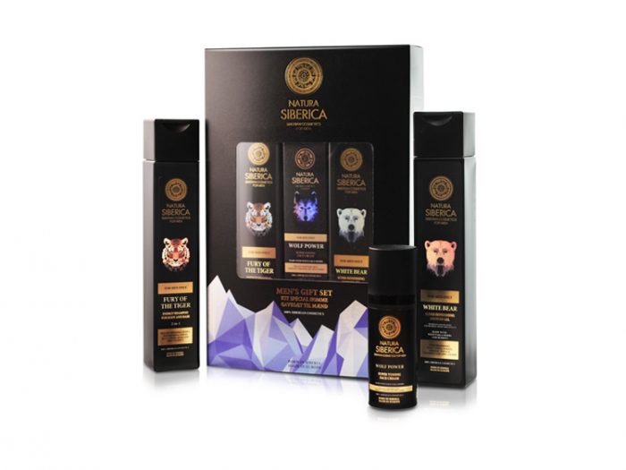 A tall rectangular black cardboard box that has Natura Siberica Men's Luxury Gift Set written in bold gold writing and some pictures of some icebergs on it next to a tall cylindrical black plastic bottle that has Natura Siberica fury of the tiger Energy Shampoo For Body & Hair written in bold gold writing and a picture of a Tiger's Face on it, a tall cylindrical black plastic bottle that has Natura Siberica white bear super refreshing shower gel written in bold gold writing and a picture of a polar bear's face on it, and a short cylindrical black plastic bottle that has Natura Siberica wolf power super toning face cream written in bold gold writing and a picture of a Wolf's face on it, on a white background.