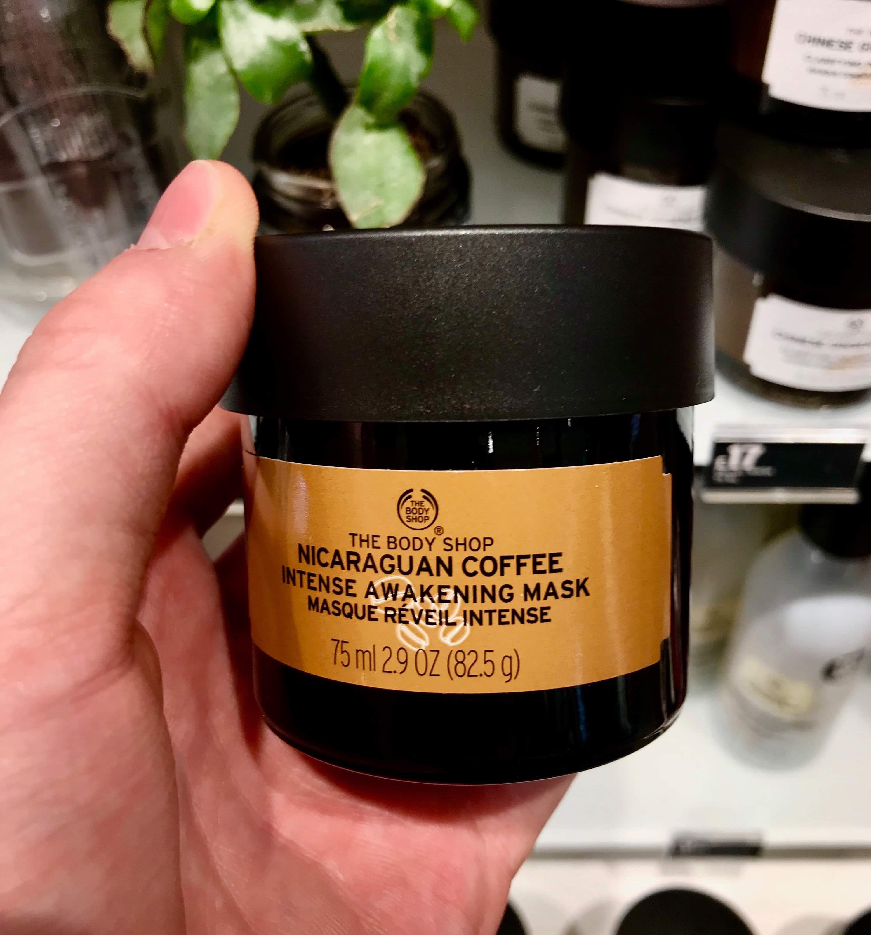 Waking Up In Nicaragua | The Body Shop Nicaraguan Coffee Intense Awakening Mask A short cylindrical clear glass jar full of some dark brown liquid with a black lid and a bright gold label that has the body shop nicaraguan coffee Intense awakening mask written in bold black writing on it, on a white background.