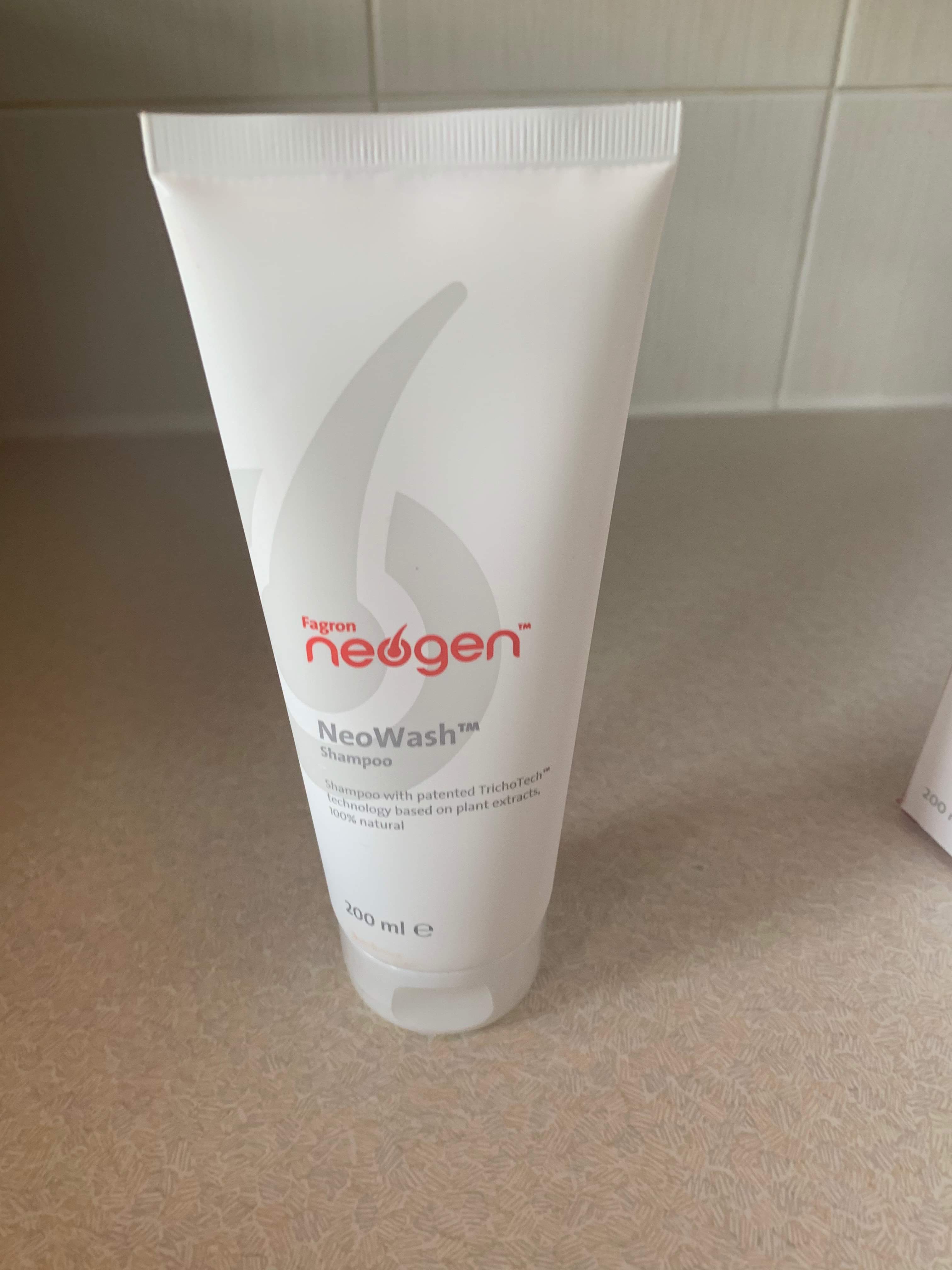 A tall conical White plastic tube that has Fagron Neogen written in bold red writing, NeoWash Hair Regenerating Shampoo written in bold grey writing, and a picture of a dark grey spiral on it, on a white background.