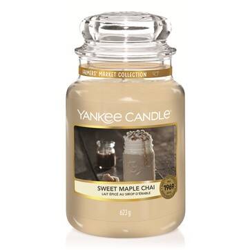 A tall glass jar full of some creamy white wax with a label that has Yankee Candle written in white writing, Sweet Maple Chai written in black writing , and a picture of a cup of frothy Chai Tea on it, on a white background.