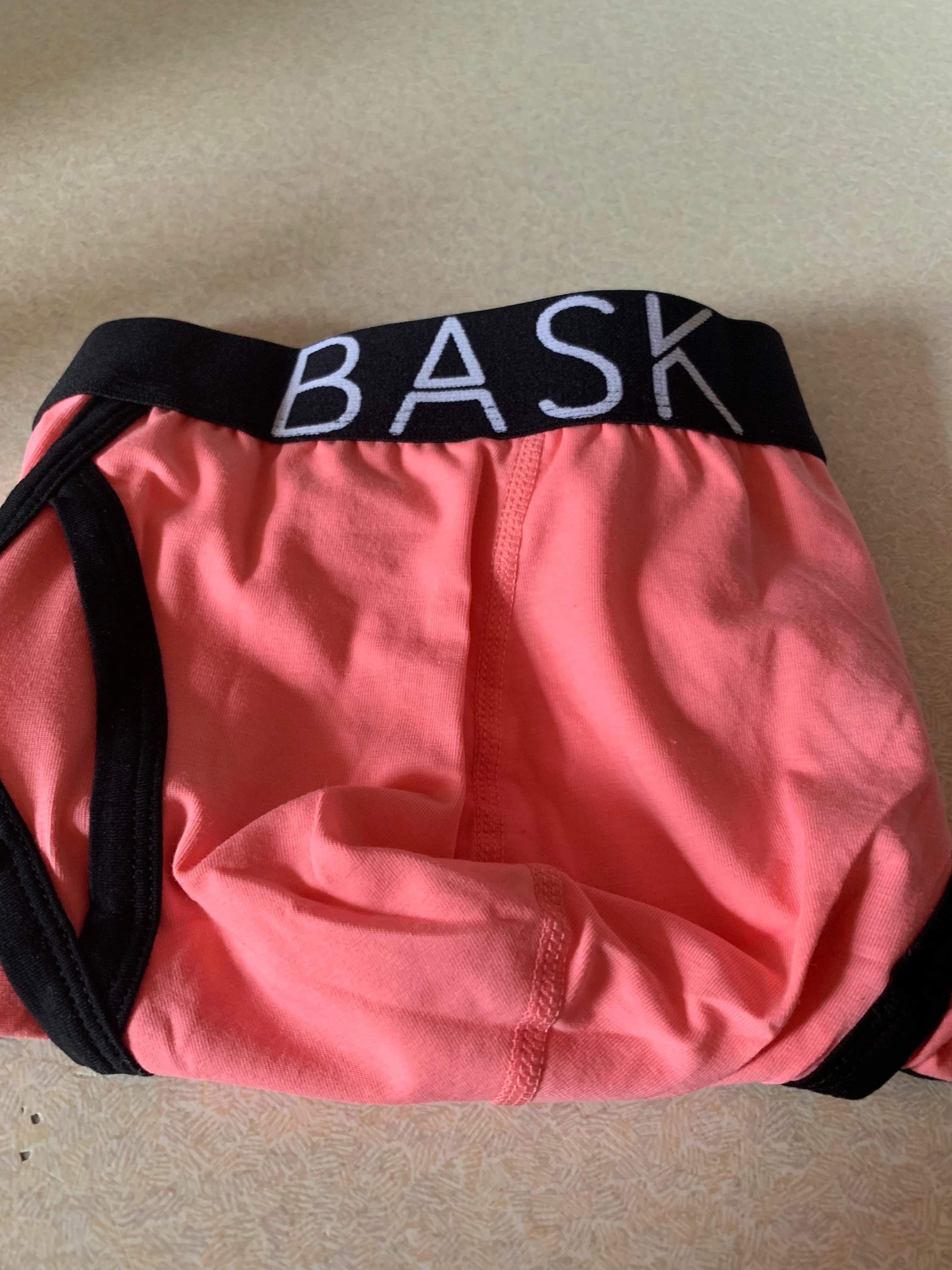 A pair of bright pink briefs with a black waistband that has Bask Menswear written in bold white writing on it, on a white background.