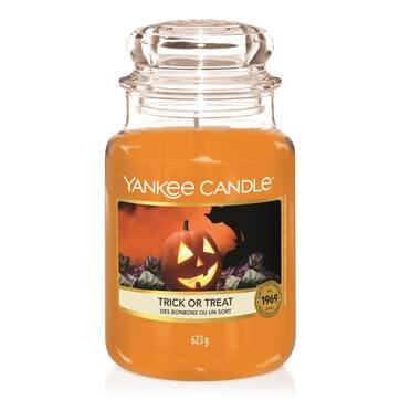 One Hell Of A Haunted Ride | Yankee Candle Halloween 2019 Collection A tall glass jar full of some bright orange wax with a label that has Yankee Candle written in white writing, Trick or Treat written in black writing, and a picture of an orange Jack-o-lantern on it, on a white background.