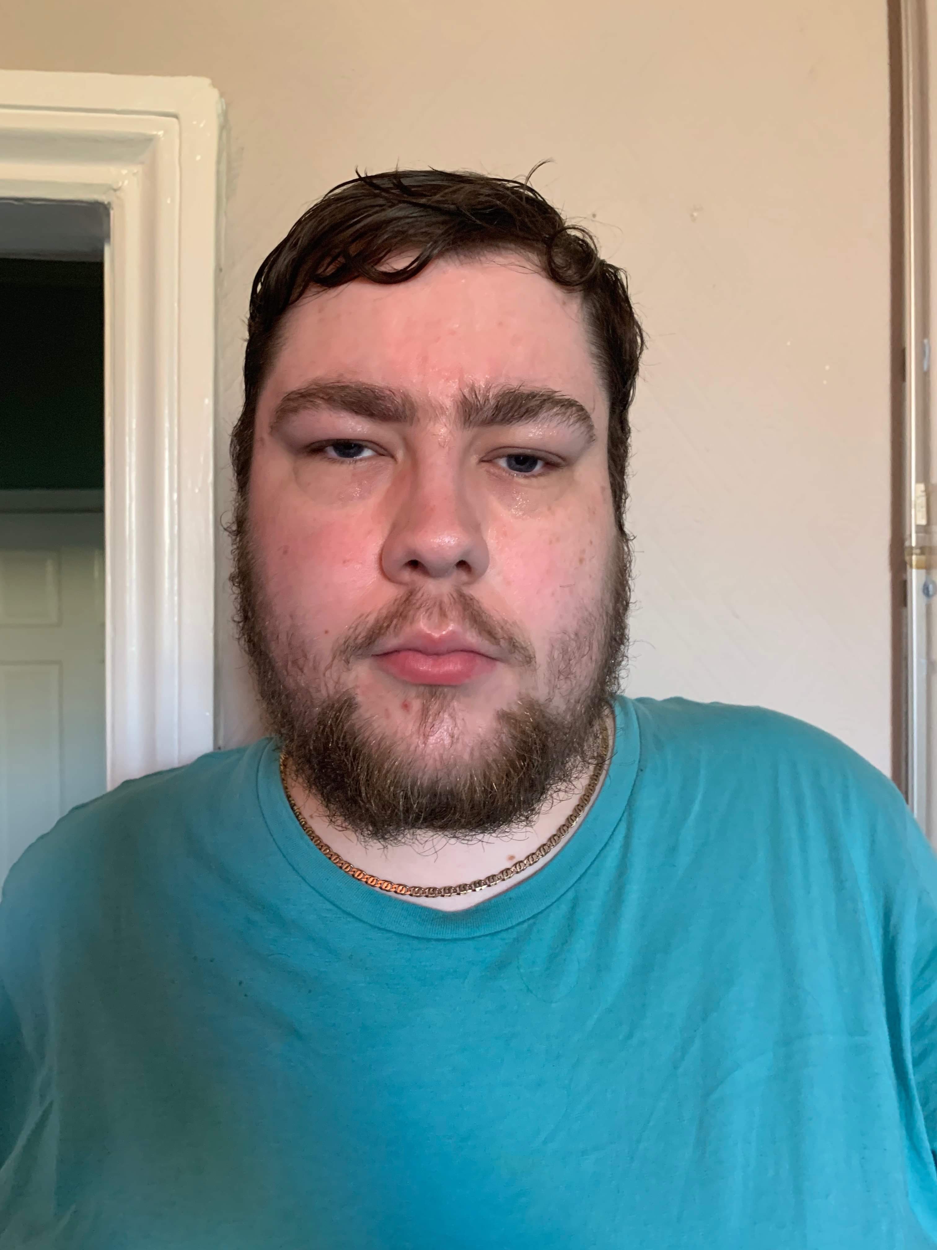 A bearded man with some oil on his face stood against a light green wall.