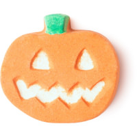 A small flat jack-o-lantern shaped bath bomb that has a white carved Face embedded on it, on a white background.