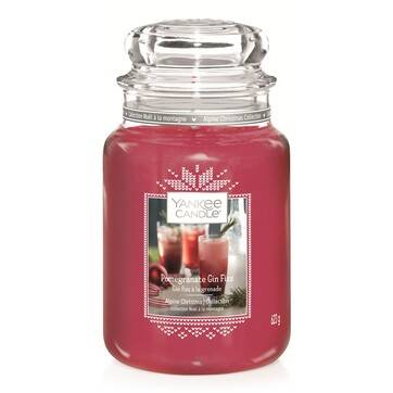 A tall glass jar full of some bright pink wax with a label that has Yankee Candle written in black writing, Pomegranate Gin Fizz written in white writing, and a picture of a tall glass full of some bright pink liquid on it, on a white background.