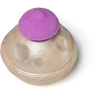 A large circular shaped bright purple bath bomb covered in some gold lustre that has a purple ufo shaped bath bomb on top of it, on a white background.