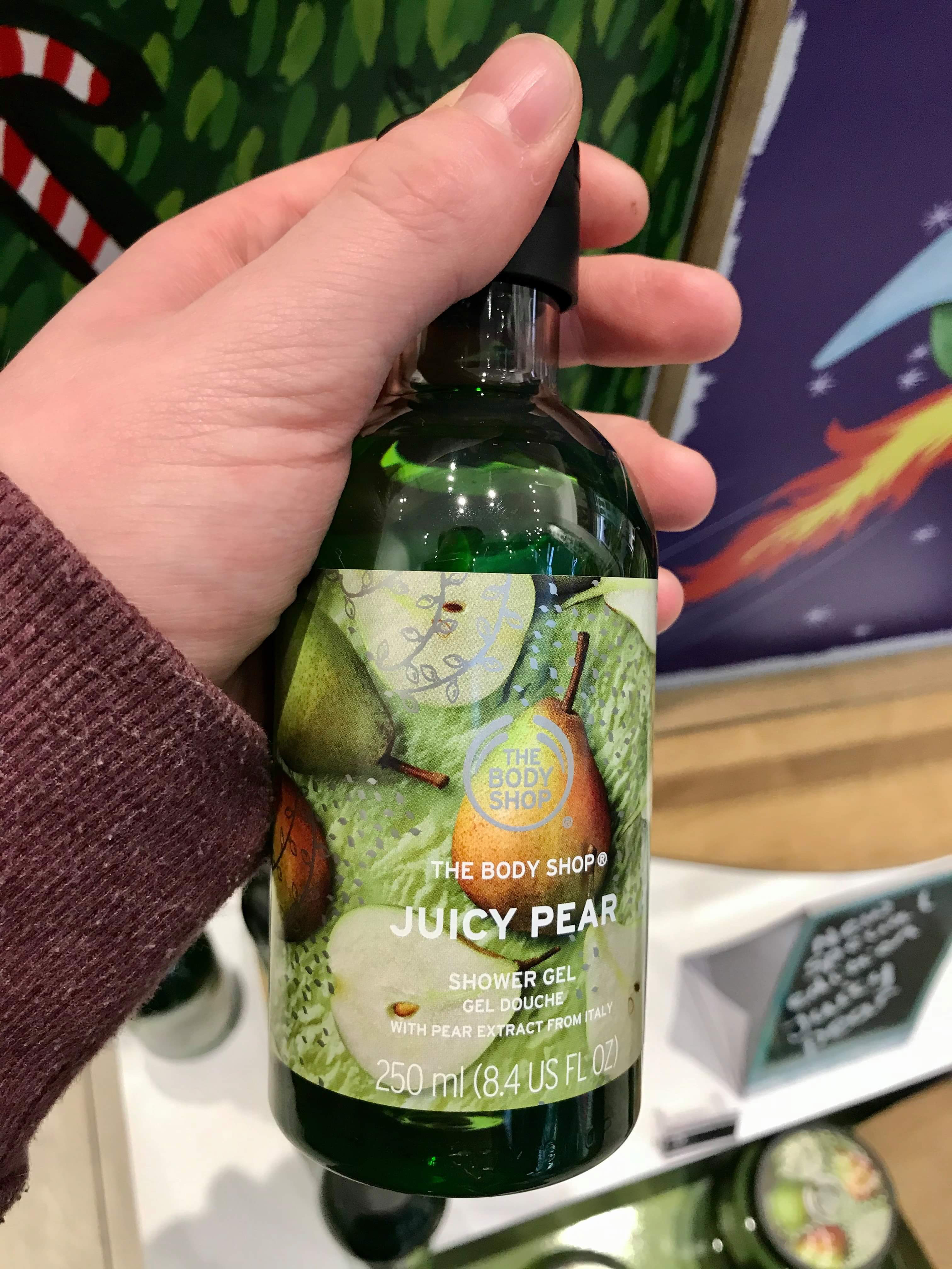 I'm Dreaming OF Soft Skin This Year | The Body Shop Christmas 2019 Range A tall cylindrical clear plastic bottle full of some dark green liquid with a black lid and a bright green label that has The Body shop juicy pear shower gel written in bold white writing and some pictures of some pears on it, on a white background.