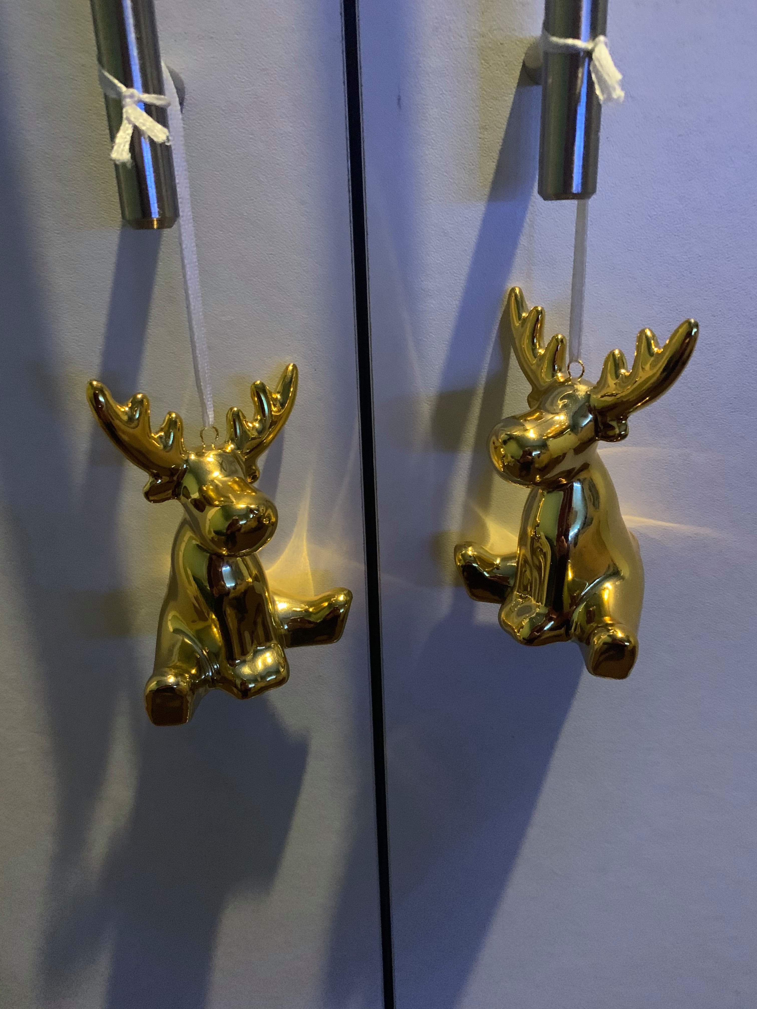 Luke Loves Christmas 2019 | How I've Decorated My Room This Year Two small gold ceramic Raindeer Ornaments wrapped around two cylindrical Silver Metal door handles on a light wooden wardrobe, on a white background.