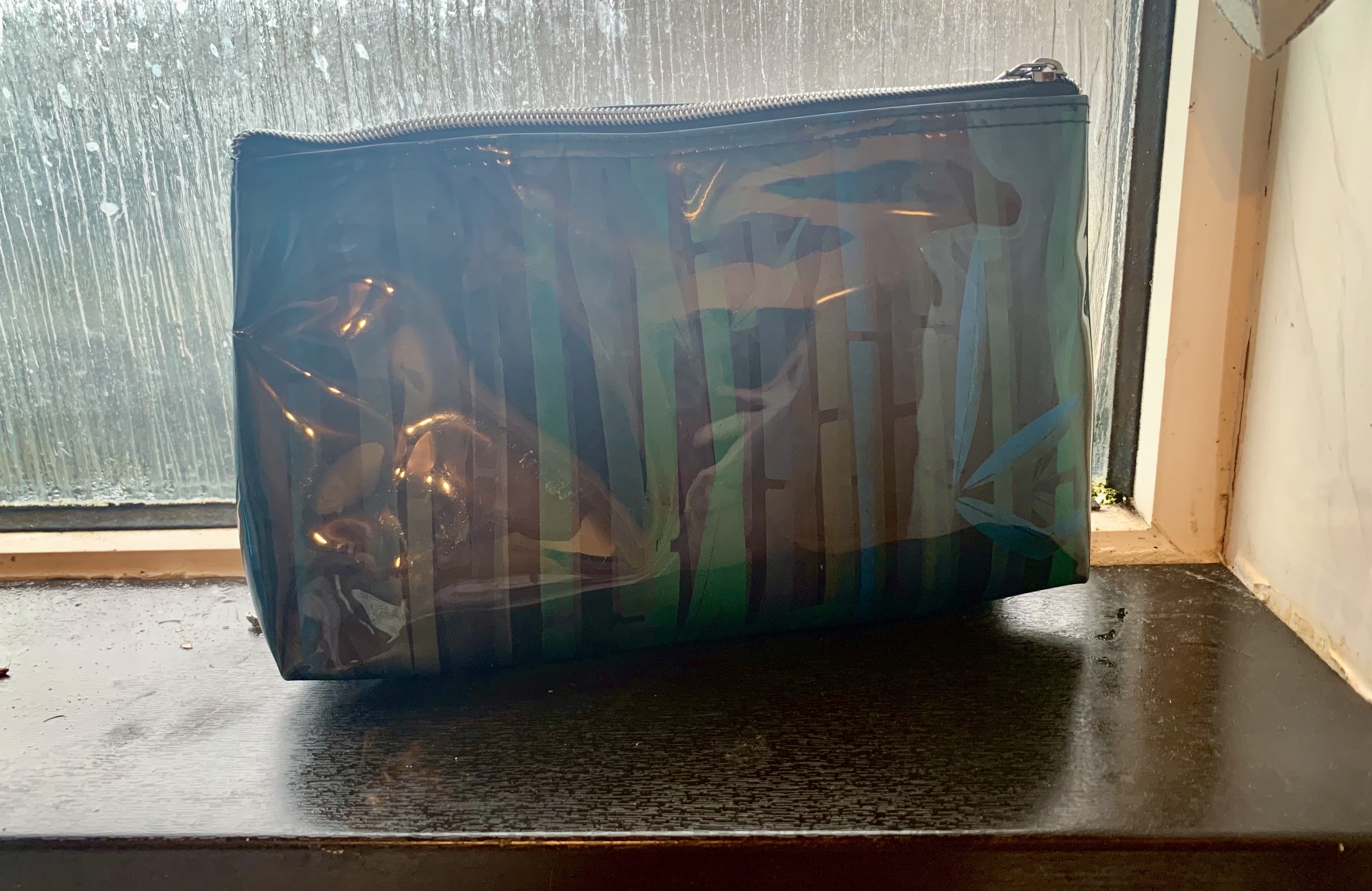 A large rectangular dark brown Bamboo and Plastic mix make up bag stood on a large rectangular white windowsill.