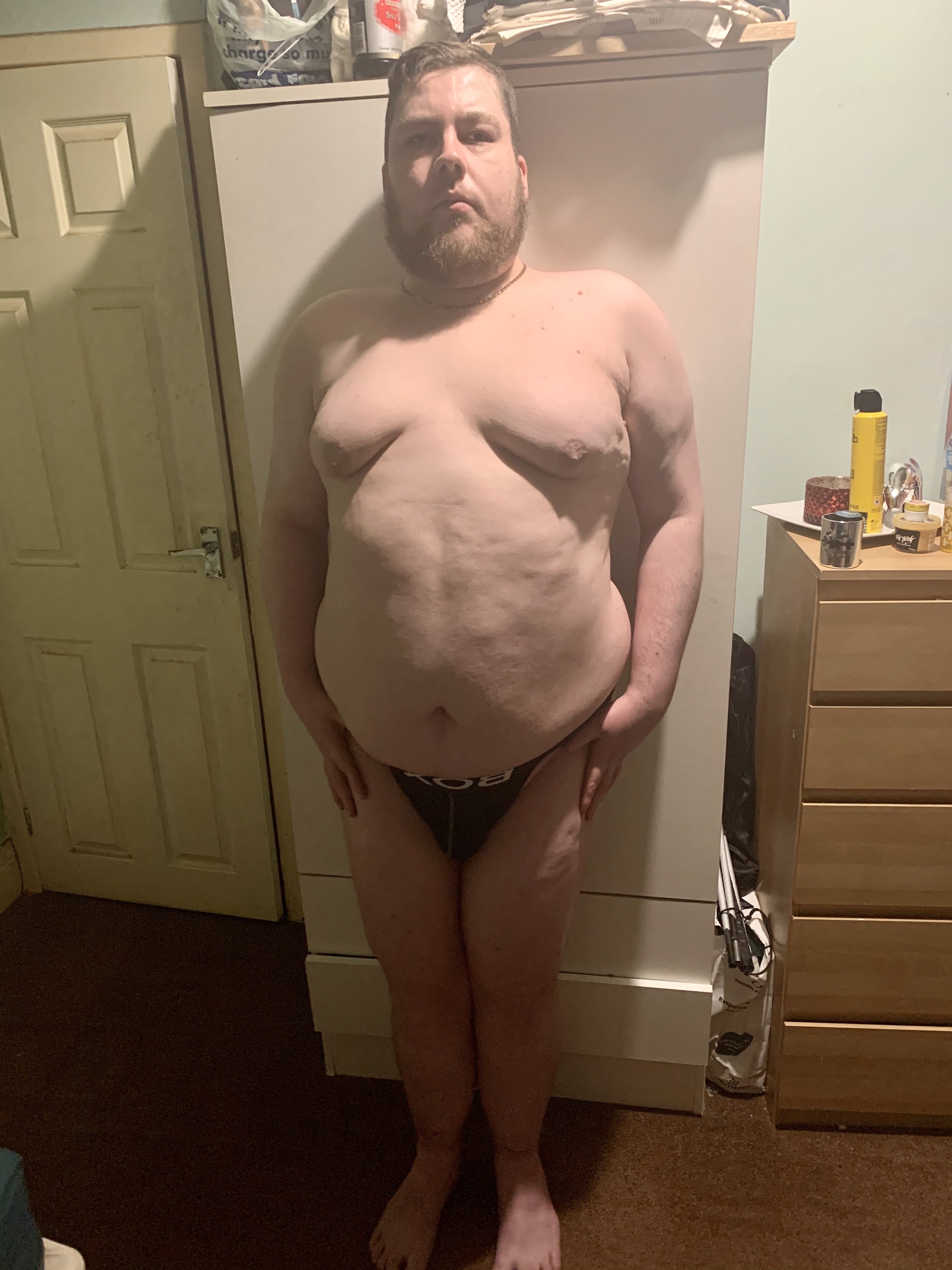 Great Underwear Fresh Out Of The Box | Box Menswear A tall bearded man wearing a black jock strap with a white waistband that has Box Menswear written in bold black writing on it stood against a light wooden wardrobe.