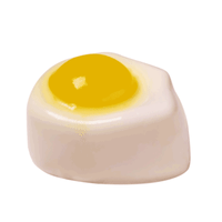 A large fried egg shaped block of shower jelly that has a bright yellow yoke on the top of it, on a white background.