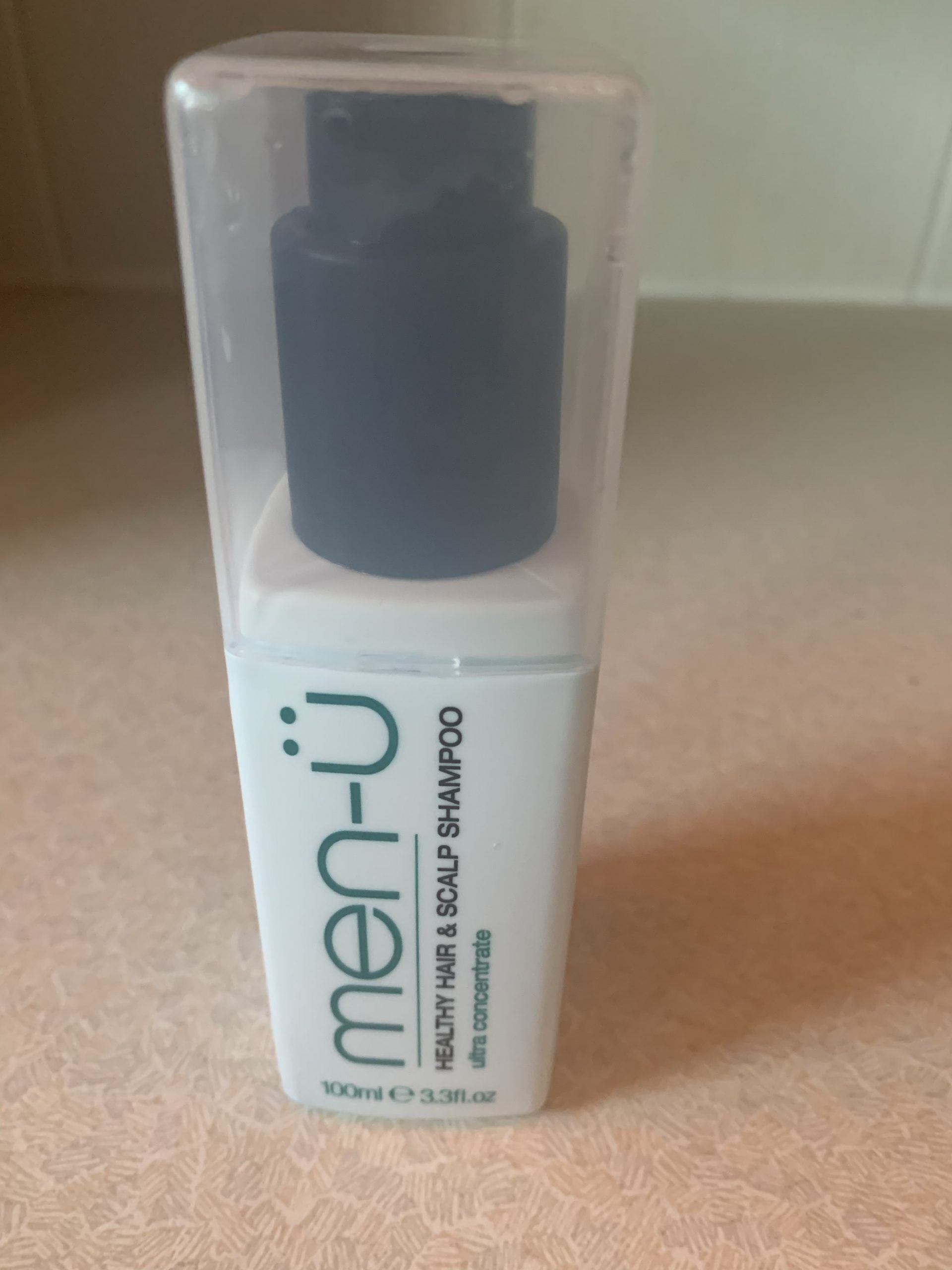 A short rectangular white plastic bottle with a clear lid that has Men-ü written in bold green writing and healthy hair & scalp shampoo written in bold black writing on it, on a white background.