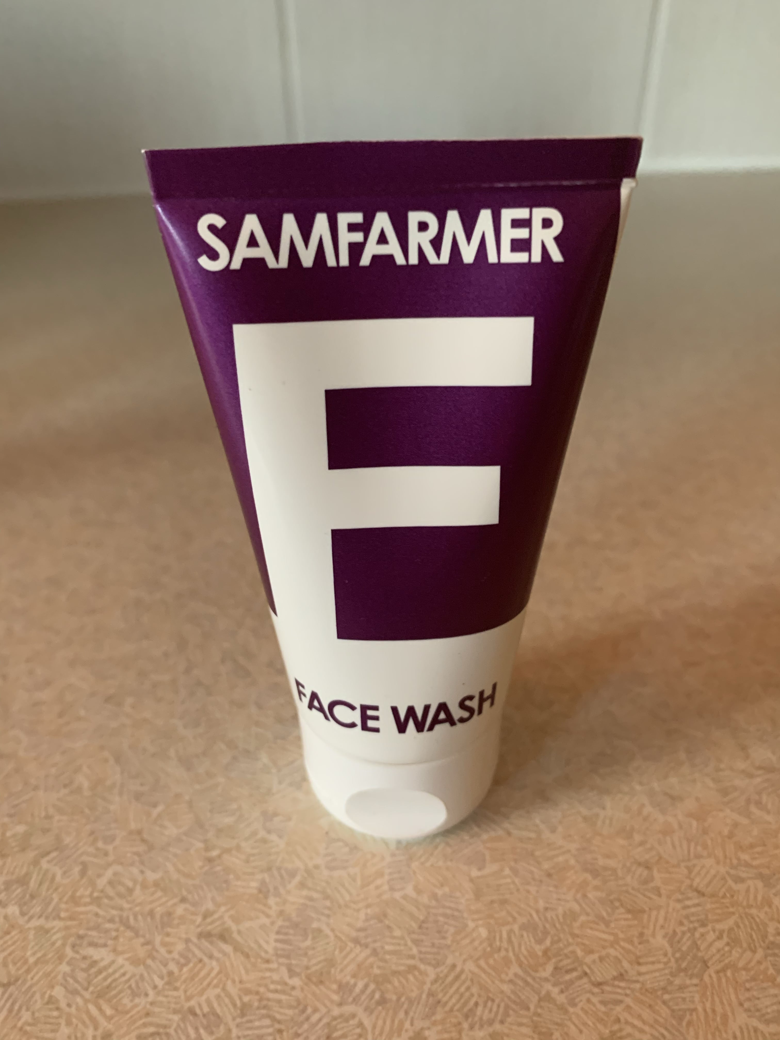 A short flat conical bright red and white plastic tube that has Sam Farmer written in bold white writing and Moisturiser written in bright red writing on it, on a white background.