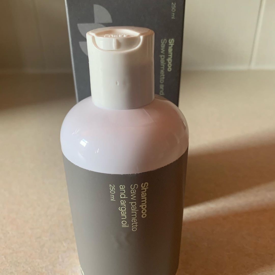 The Son Won't See Anymore Bald Spots | Sons DHT Blocker Shampoo | Gifted A tall wide cylindrical white plastic bottle with a light grey label that has Sons DHT Blocker Shampoo written in bold white writing on it next to a tall white cardboard box that has Sons DHT Blocker Shampoo written in bold black writing on it, on a white background.