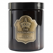 A short cylindrical amber coloured glass jar full of some bright white wax with a black lid and a black label that has The Imaginarium Sherbet Lemons Candle written in bold gold writing on it, on a white background.