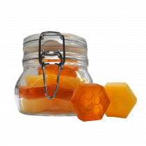 A large octagonal shaped glass mason jar full of some small different coloured honeycomb shaped soaps with a silver metal lever clasp, on a white background..