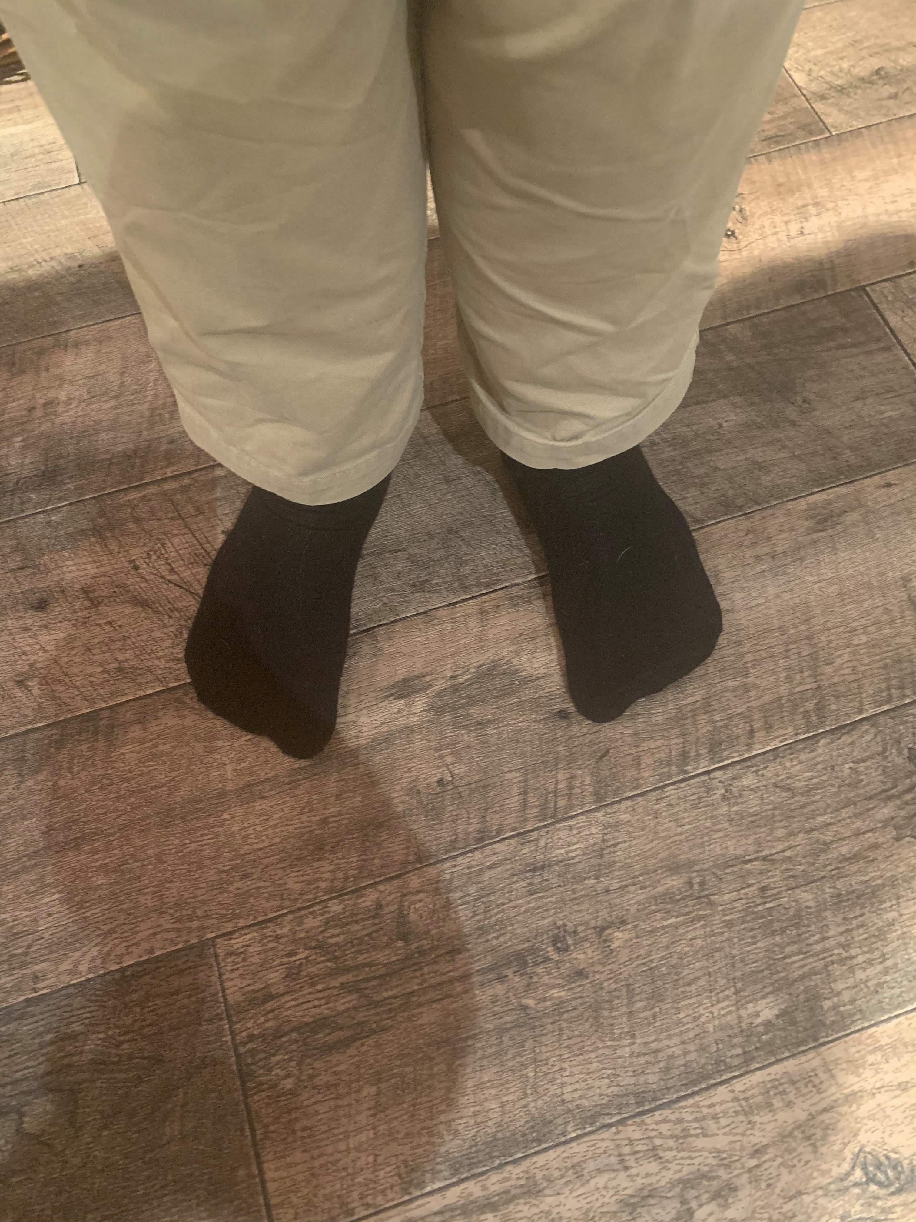 Me wearing a pair of thick black socks on a light wooden laminate floor.