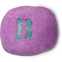 Fairytales Are Real | Lush Unicorn Horn Bubble Bar and Prince Charming Shower Cream A small bright purple oval bubble bar that has a bright green glitter letter B engraved on top of it, on a white background.