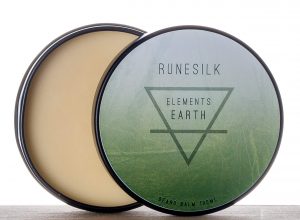 A short cylindrical silver and metallic green open tin full of some creamy white Beard Balm that has Runesilk Elements Earth Beard Balm written in bold black writing and a picture of a black triangle on it, on a white background.