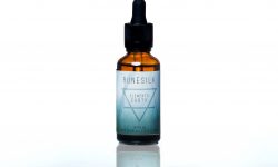 A short cylindrical brown glass bottle with a black rubber pipette lid and a white and gradient green label that has runesilk elements earth beard oil written in bold black writing and a picture of a black triangle on it, on a white background.