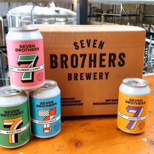 A large rectangular cardboard box that has Seven Bro7hers Mixed Core 12 Pack written in bold black writing on it next to a selection of short cylindrical metal beer cans that all have Seven Bro7hers written in bold black writing on them, on a white background.