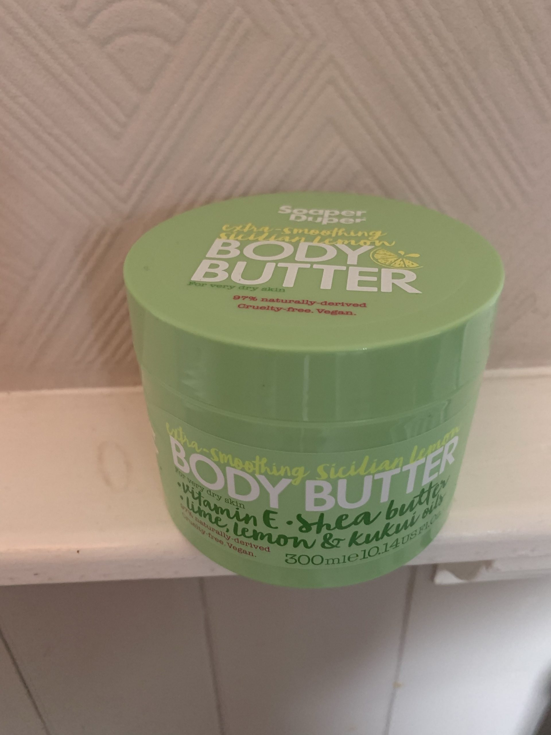 A short wide cylindrical bright green plastic tub that has Soaper Duper Extra Smoothing Sicilian Lemon Body Butter written in bold white writing on it, on a white background.