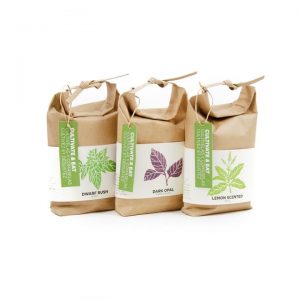 Three small rectangular brown paper seed packets that have Lemon Scented Basil, Dark Opal Purple Basil, and Dwarf Bush Basil written in bold black writing and some pictures of some different coloured leaves on them, on a white background.