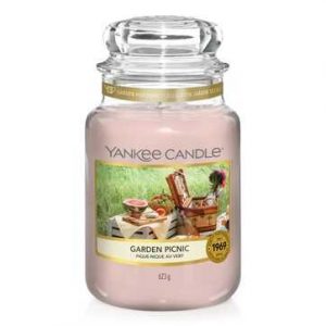 A tall glass jar full of some pale pink wax with a label that has Yankee Candle written in black writing, Garden Picnic written in black writing, and a picture of a picnic blanket in a field on it, on a white background.