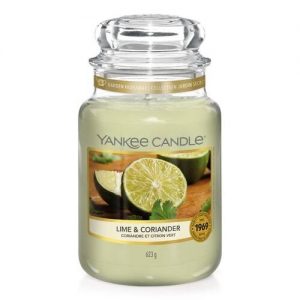 A tall glass jar full of some bright green wax with a label that has Yankee Candle written in black writing, Lime & Coriander written in black writing, and a picture of half a lime and some coriander leaves on it, on a white background.