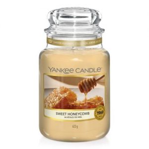 A tall glass jar full of some creamy white wax with a label that has Yankee Candle written in black writing, Sweet Honeycomb written in black writing, and a picture of a large block of golden honeycomb on it, on a white background.