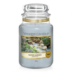 A tall glass jar full of some pale blue blue wax with a label that has Yankee Candle written in black writing, water garden written in black writing, and a picture of a babbling stream on it, on a white background.