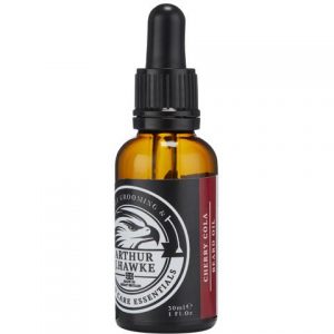 A short cylindrical dark green glass bottle with a black rubber pipette lid and a black label that has Arthur J Hawke Cherry Cola Beard Oil written in bold white writing on it, on a white background.