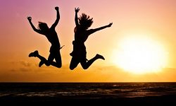 Some silhouettes of two excited people jumping in front of a bright orange Sunset.