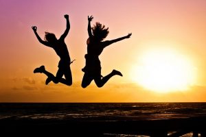 Some silhouettes of two excited people jumping in front of a bright orange Sunset.