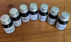 A collection of seven short cylindrical clear glass jars full of some clear liquid with white labels that all have The Perfume People written in bold black writing on them, on a white background.