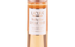 A tall cylindrical clear plastic bottle full of some translucent gold liquid with a bright gold lid that has Aldi Lacura Healthy Glow Glycolic Toner written in bold black writing on it, on a white background.