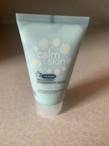 A short fat conical light green plastic tube that has Superdrug written in bold black writing, Calm Skin Overnight Face Mask written in bold white writing, and some pictures of some white chamomile petals on it, on a white background.