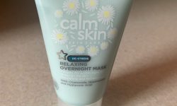 A short fat conical light green plastic tube that has Superdrug written in bold black writing, Calm Skin Overnight Face Mask written in bold white writing, and some pictures of some white chamomile petals on it, on a white background.