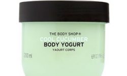 A short rounded rectangular clear plastic tub full of some pale turquoise liquid with a dark green lid that has The Body Shop Cool Cucumber Body Yoghurt written in dark green writing and some pictures of some bright green cucumbers on it, on a white background.