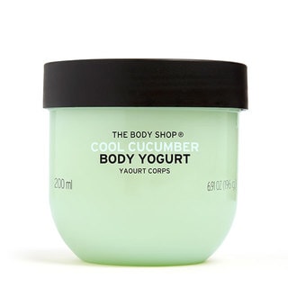 A short rounded rectangular clear plastic tub full of some pale turquoise liquid with a dark green lid that has The Body Shop Cool Cucumber Body Yoghurt written in dark green writing and some pictures of some bright green cucumbers on it, on a white background.