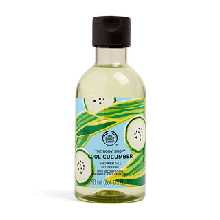 A tall cylindrical clear plastic bottle full of some pale turquoise liquid with a dark green lid and a bright green label that has The Body Shop Cool Cucumber Shower Gel written in dark green writing and some pictures of some bright green cucumbers on it, on a white background.