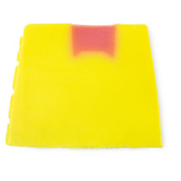 A large trapezium shaped block of bright yellow and orange dotted soap that has Lush engraved in the side of it, on a white background.